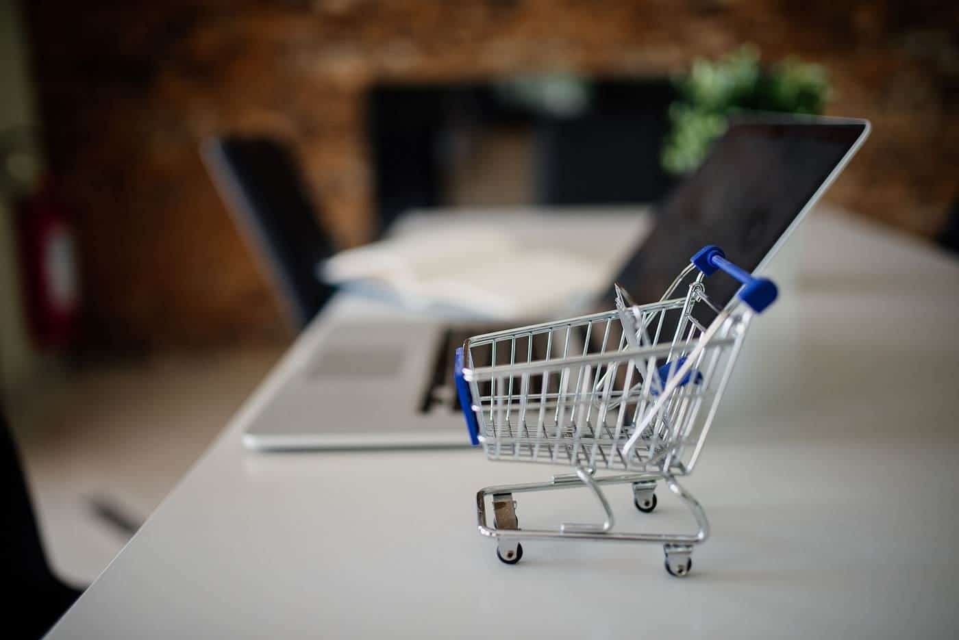 A miniature shopping trolley on a desk next to an open laptop
