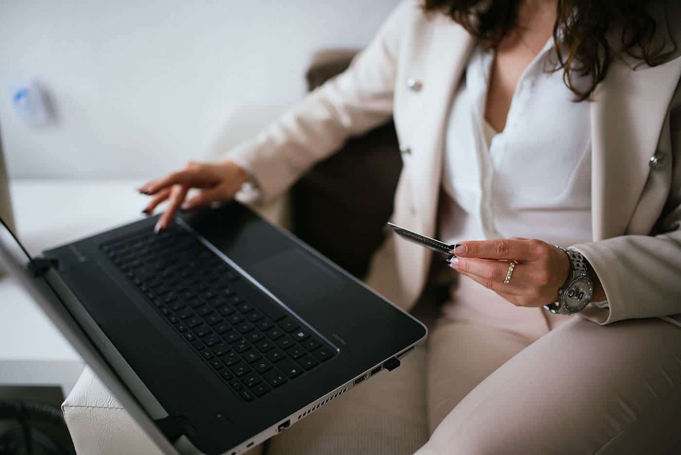 A person at a home desk using a laptop while holding a payment card