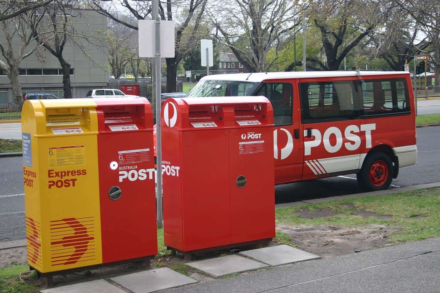 Red Australian post boxes on a footpath with a delivery van parked behind