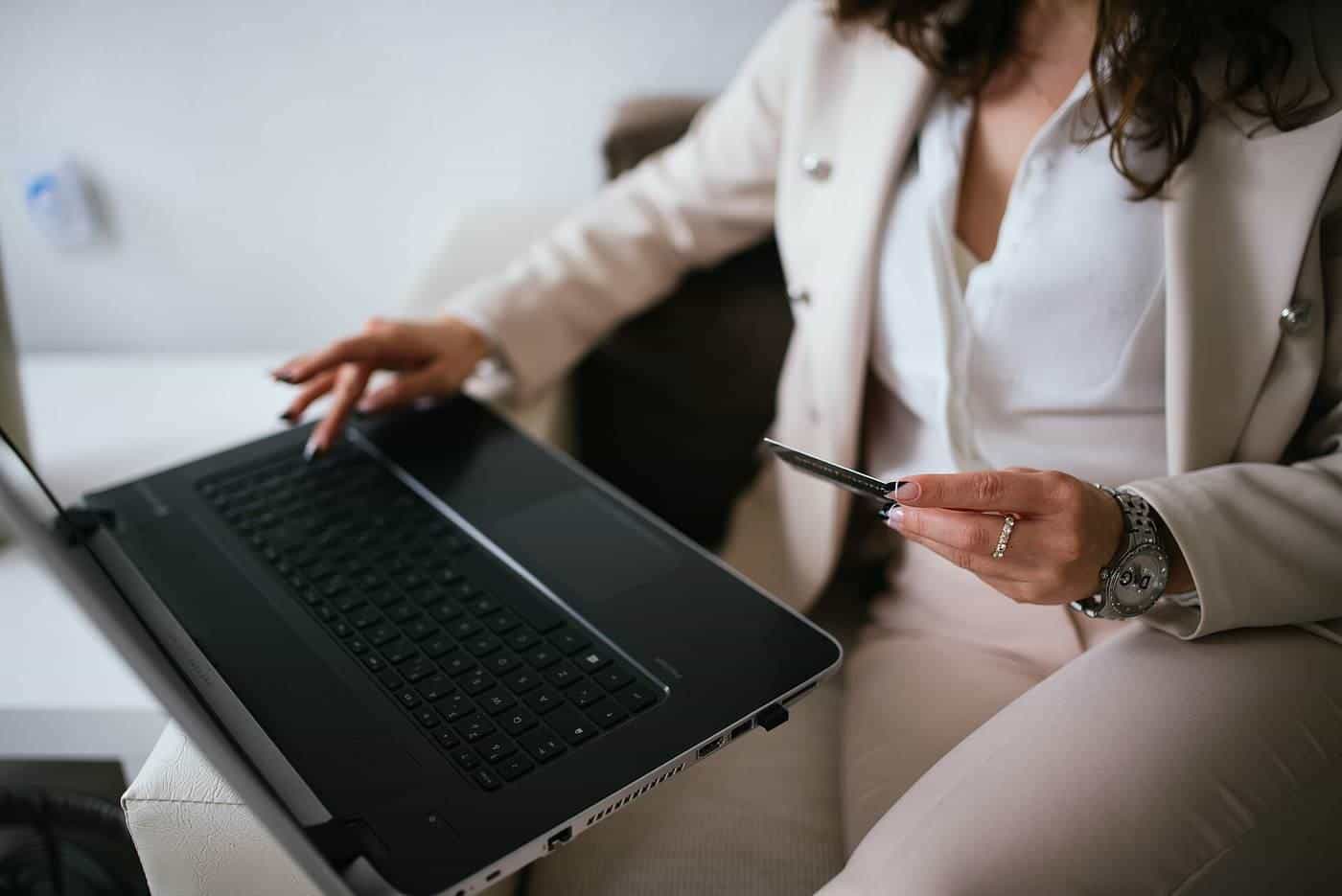 A person at a home desk using a laptop while holding a payment card